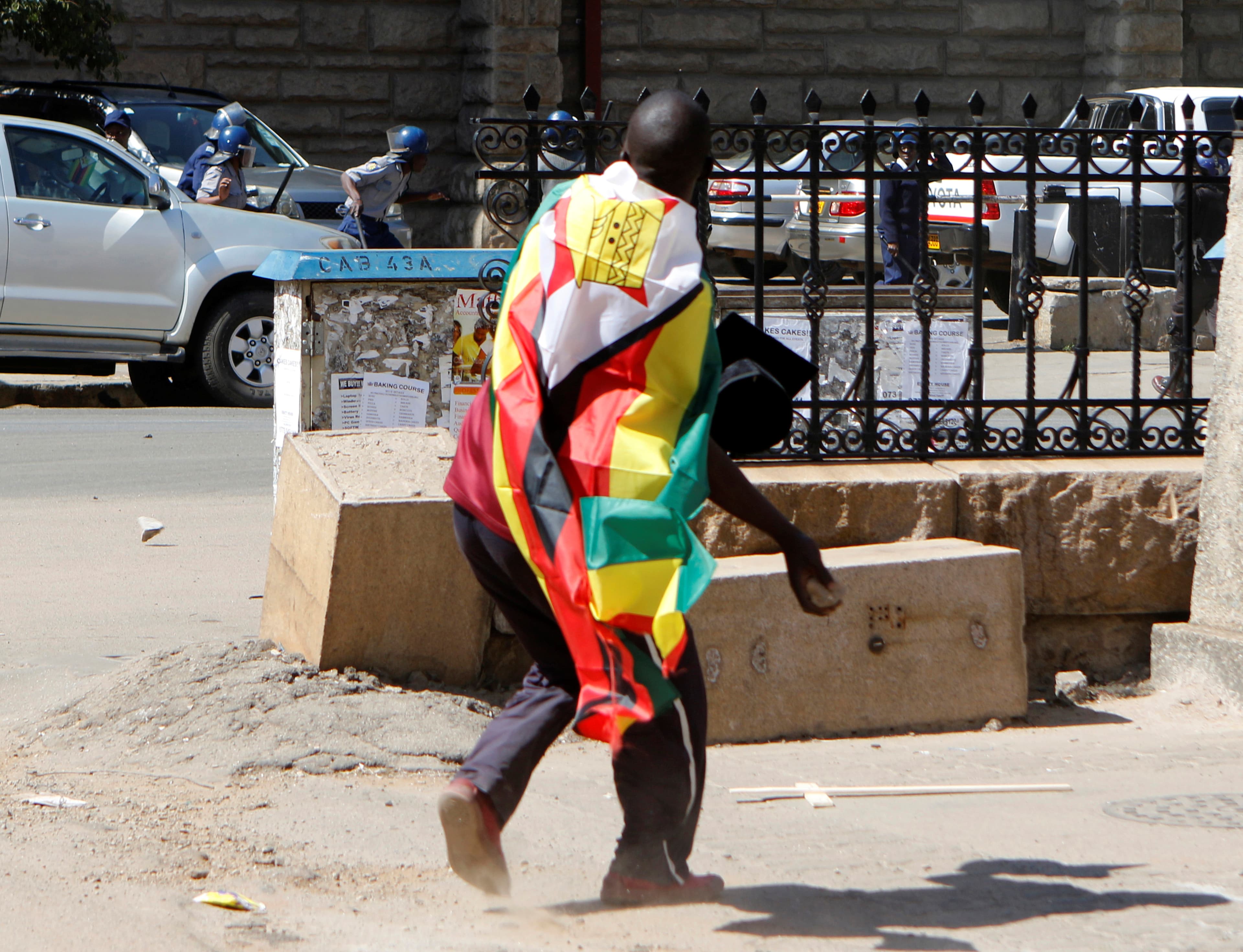 A man with a Zimbabwean flag wrapped around him throws stones