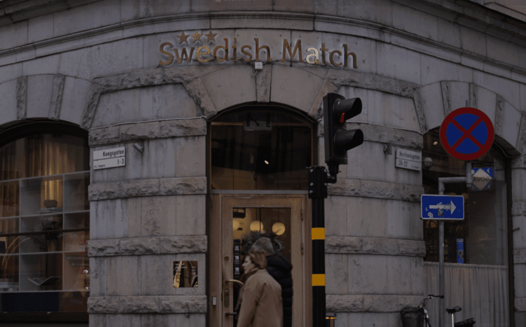 A street corner with a building labeled 'Swedish Match' above an entrance door; traffic signs and a traffic light are visible in the foreground.