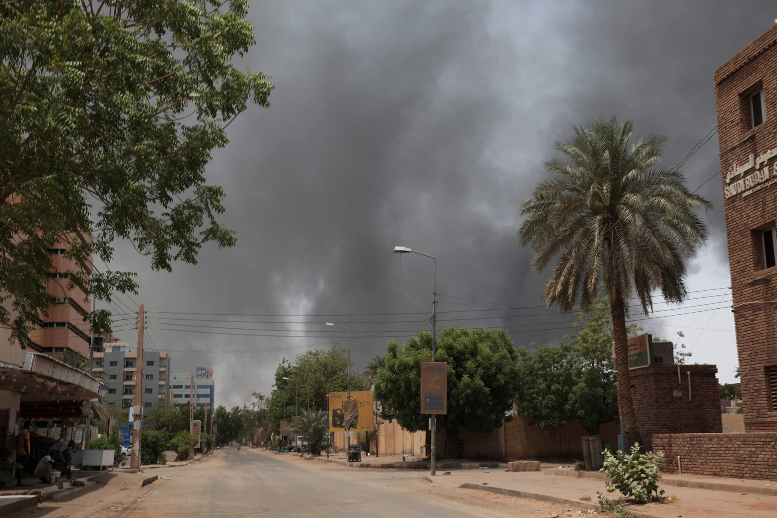 A deserted street lined with trees and buildings under a sky filled with thick, dark smoke.