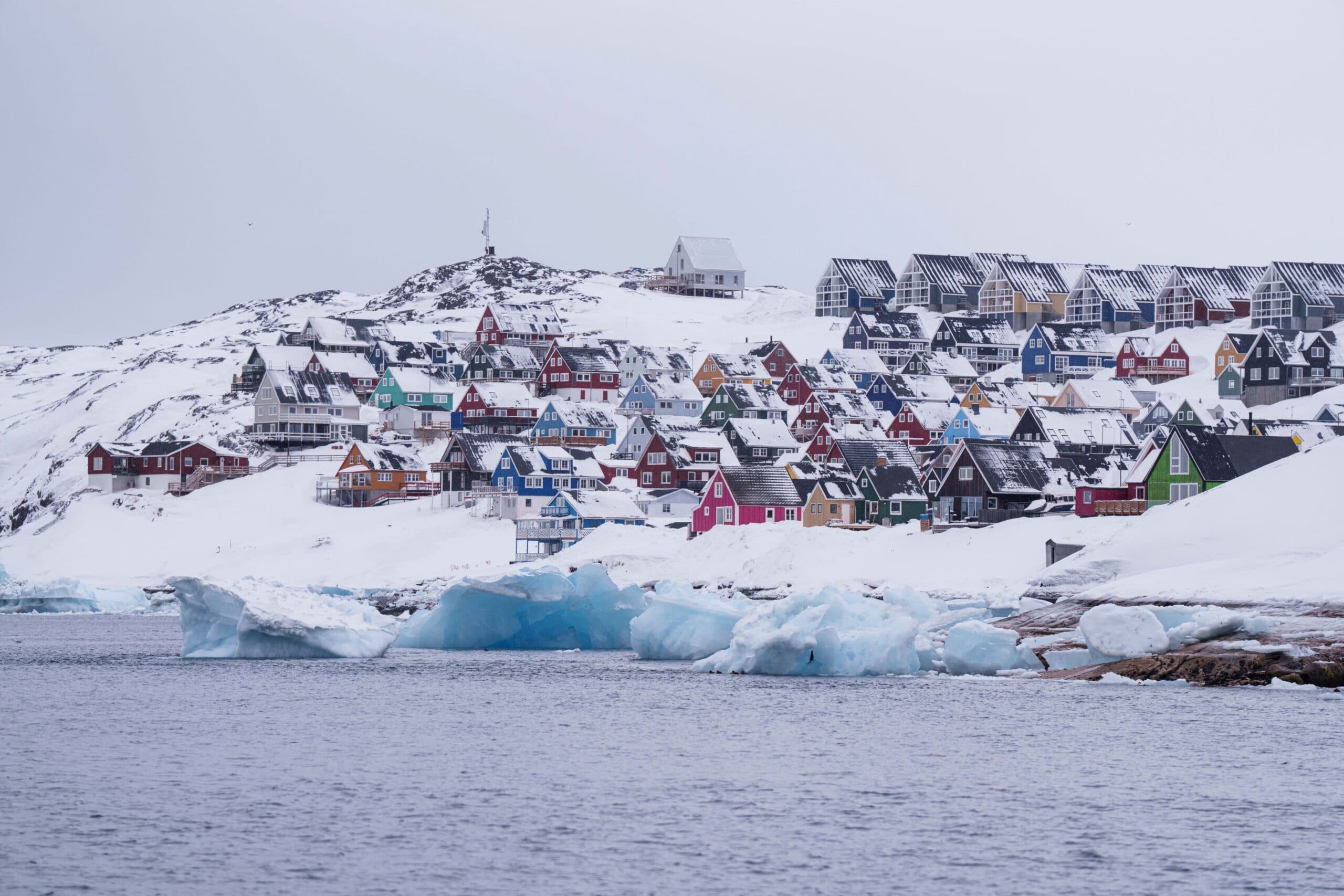 Colorful houses in a snowy village by the sea, with icebergs floating in the water.