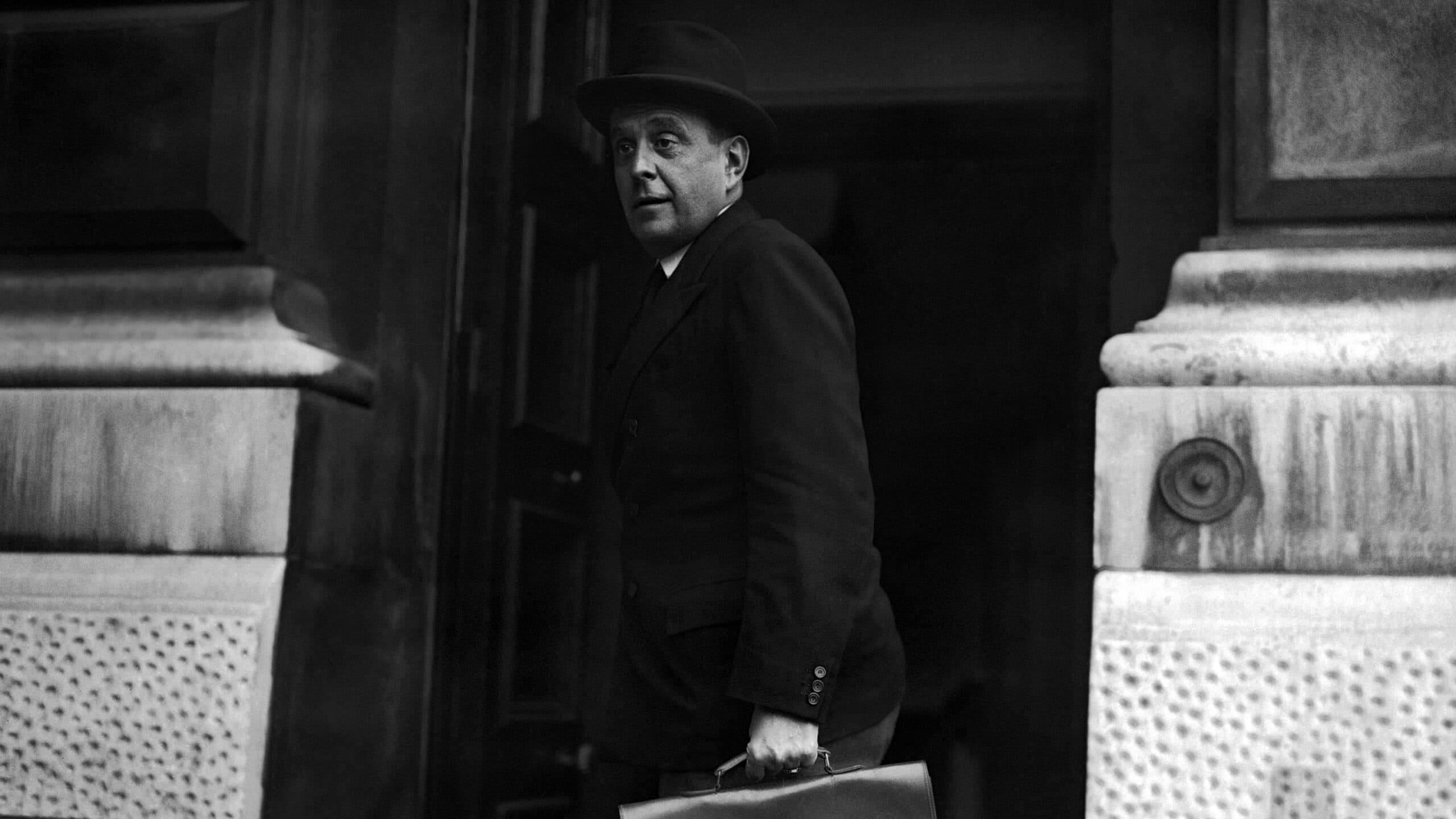 A man in a suit and bowler hat is stepping out of a building while carrying a briefcase.