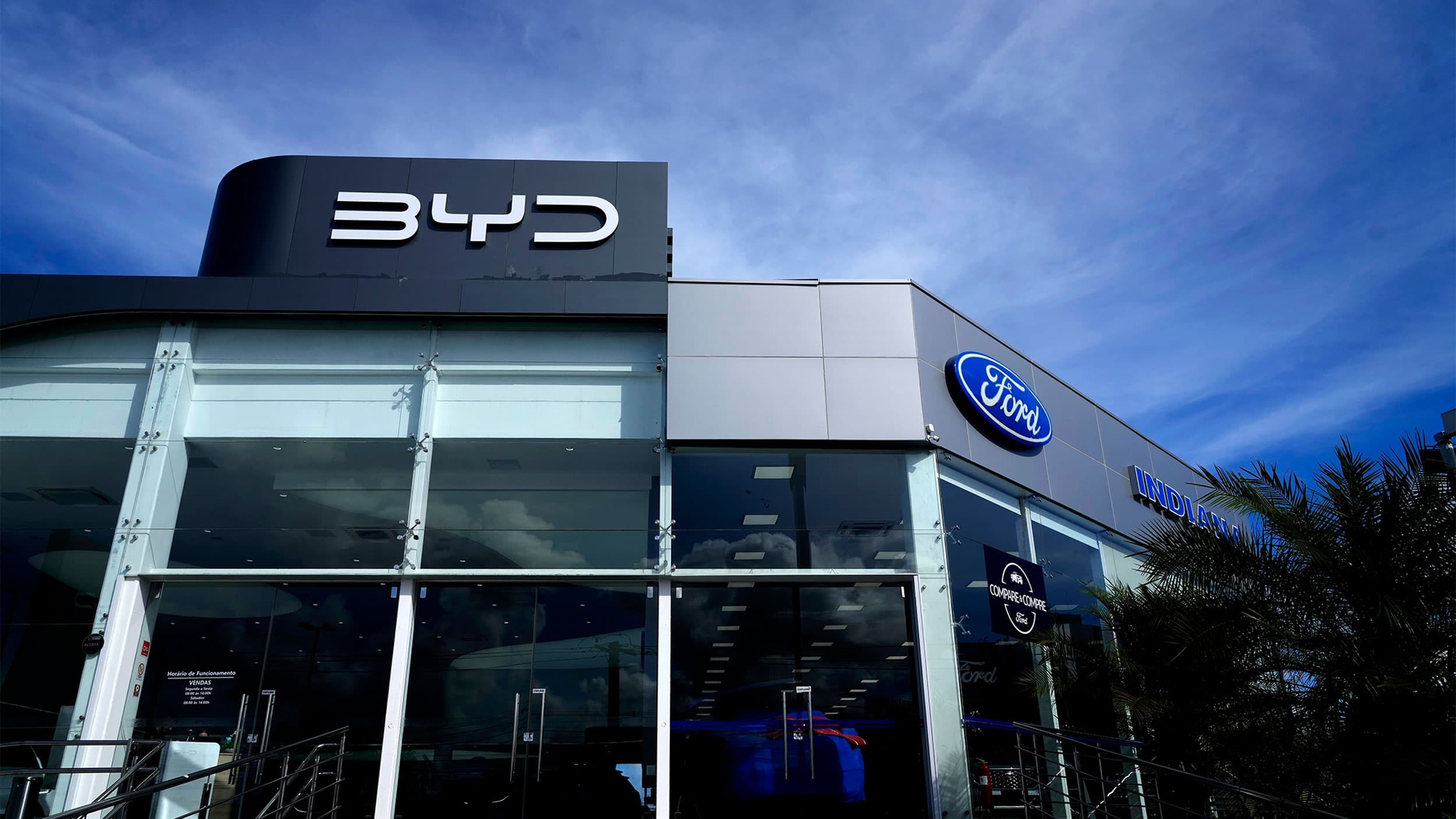 A car dealership building featuring logos of BYD and Ford on its facade, with a clear blue sky above.