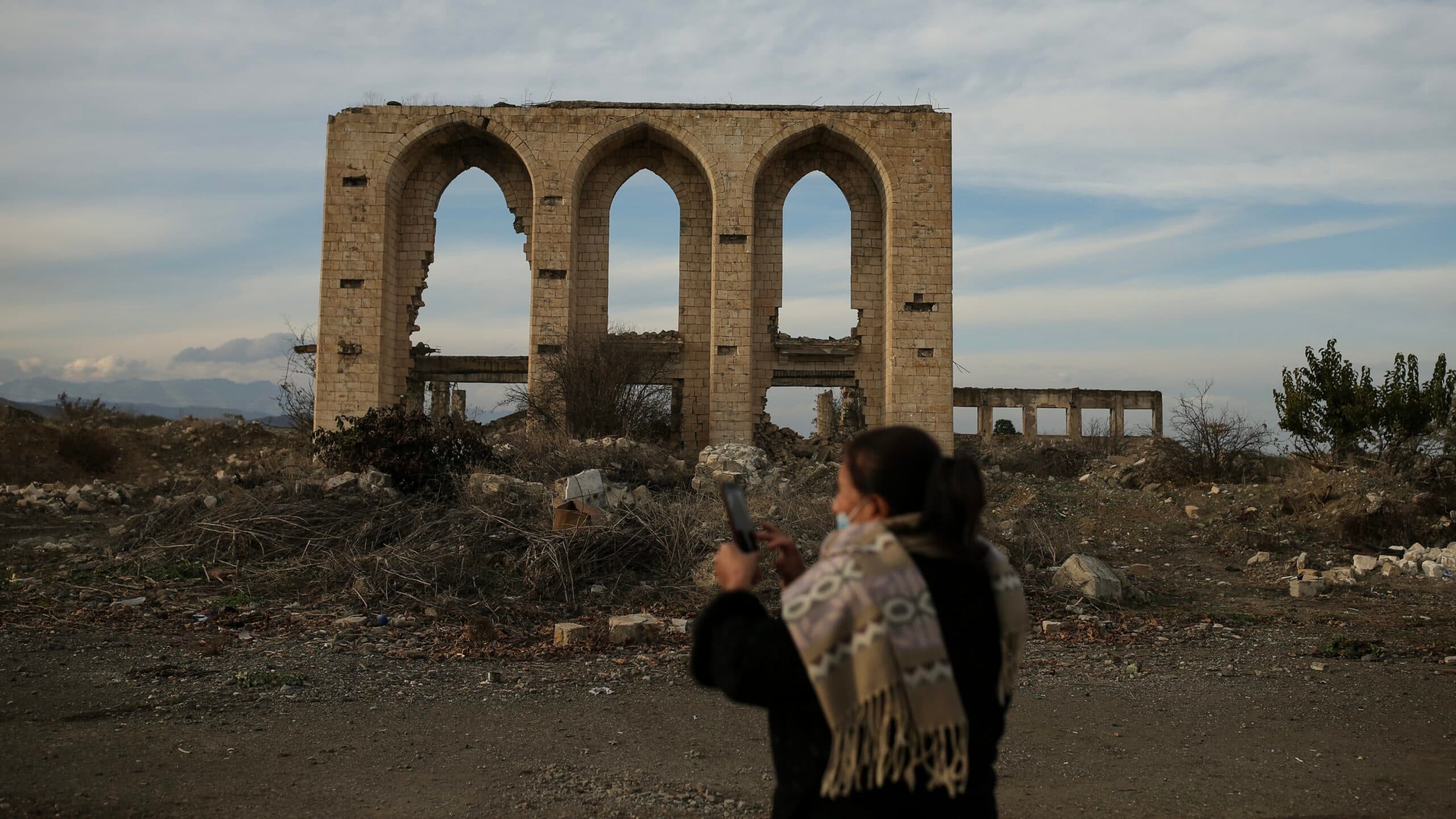 A person taking a photo of a large, ancient stone archway ruin in a desolate landscape.