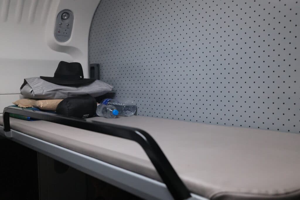 A simple train sleeper berth with a hat, pillows, and water bottles placed on it.