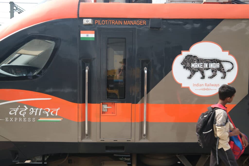 A person walks past the side of an Indian train with a "Make in India" logo and the Indian flag visible.