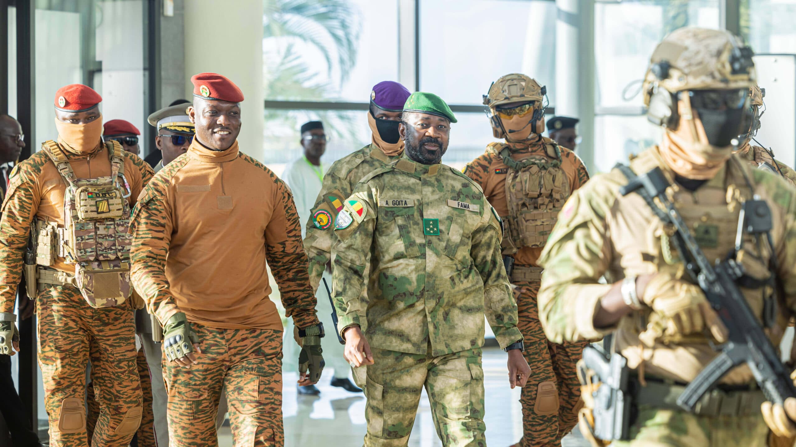 A group of people in military uniforms walking indoors, with a mix of camouflage and orange-brown patterns.