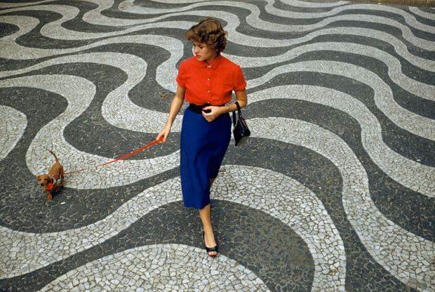 A woman walks a dachshund across pavement with undulating wave patterns in Rio de Janeiro, Brazil, March 1955. (Photograph by Charles Allmon, National Geographic)