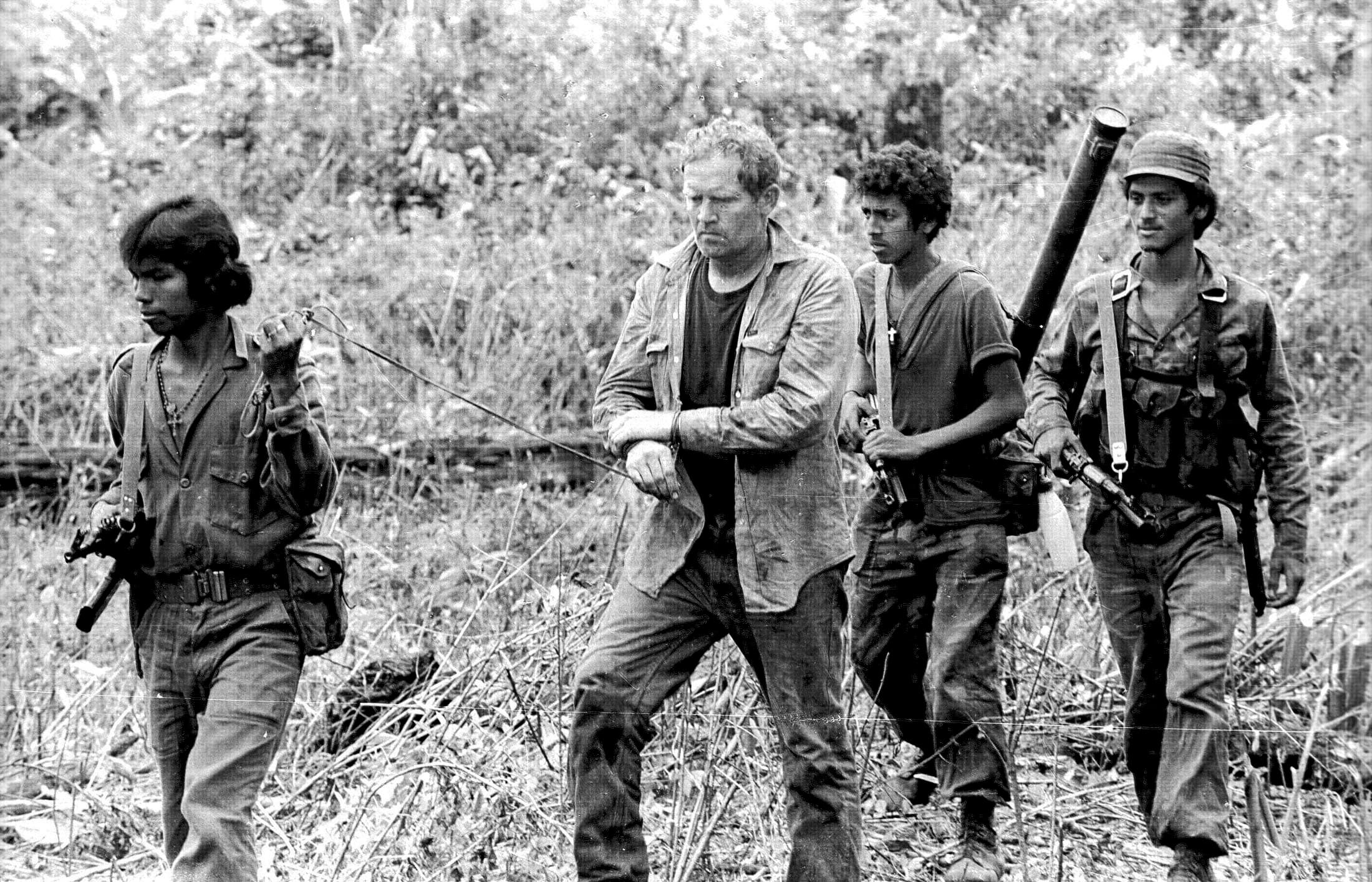 One solider leads an American pilot with hands tied while two soldiers follow behind