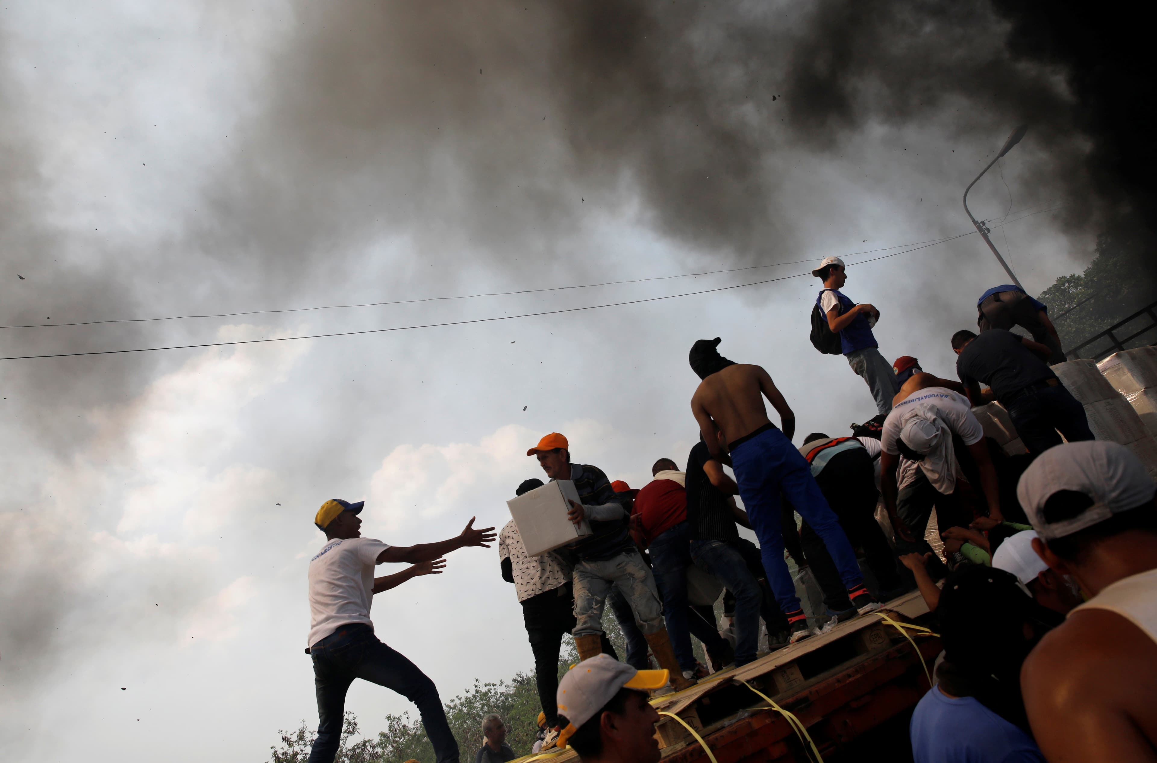 With smoke in the background, men pass boxes to each other on a truck.