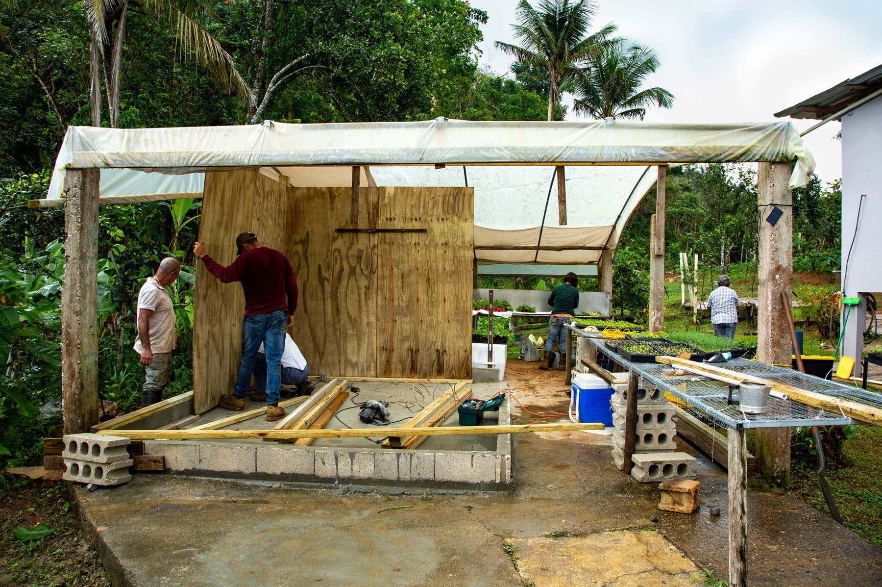Three men are show putting up a ply board piece of wood that will be one of the walls of a storage unit.
