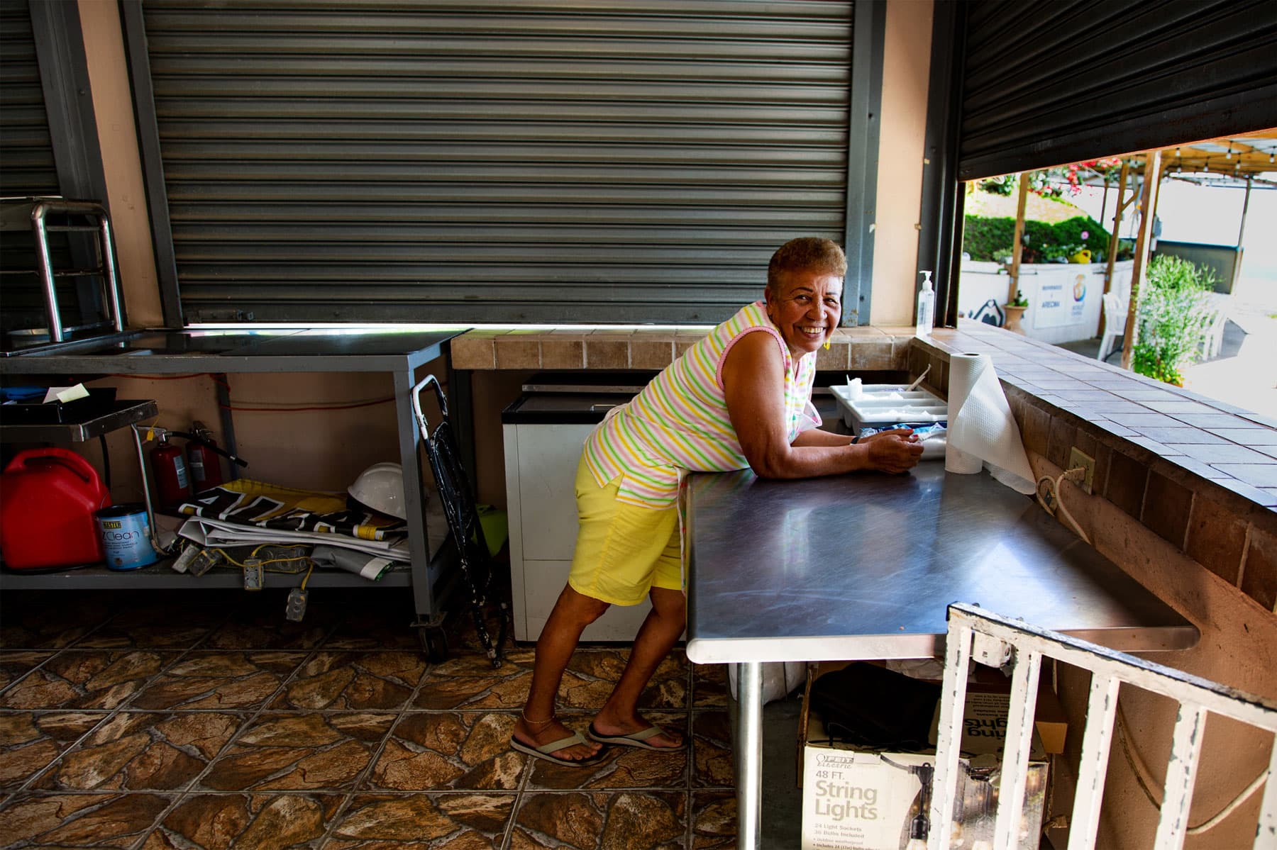 A woman in yellow shorts and s striped shirt leans toward an open service window.