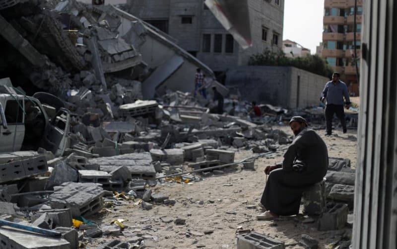 A man sits looking at a building in ruins.
