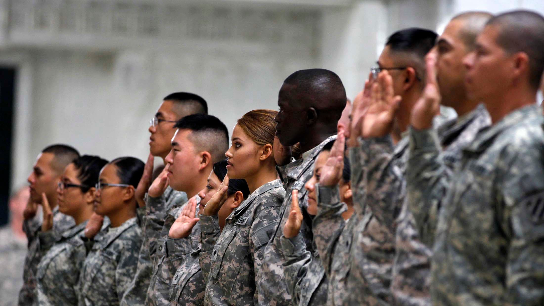 A line of soldiers in fatigues hold up their right hand