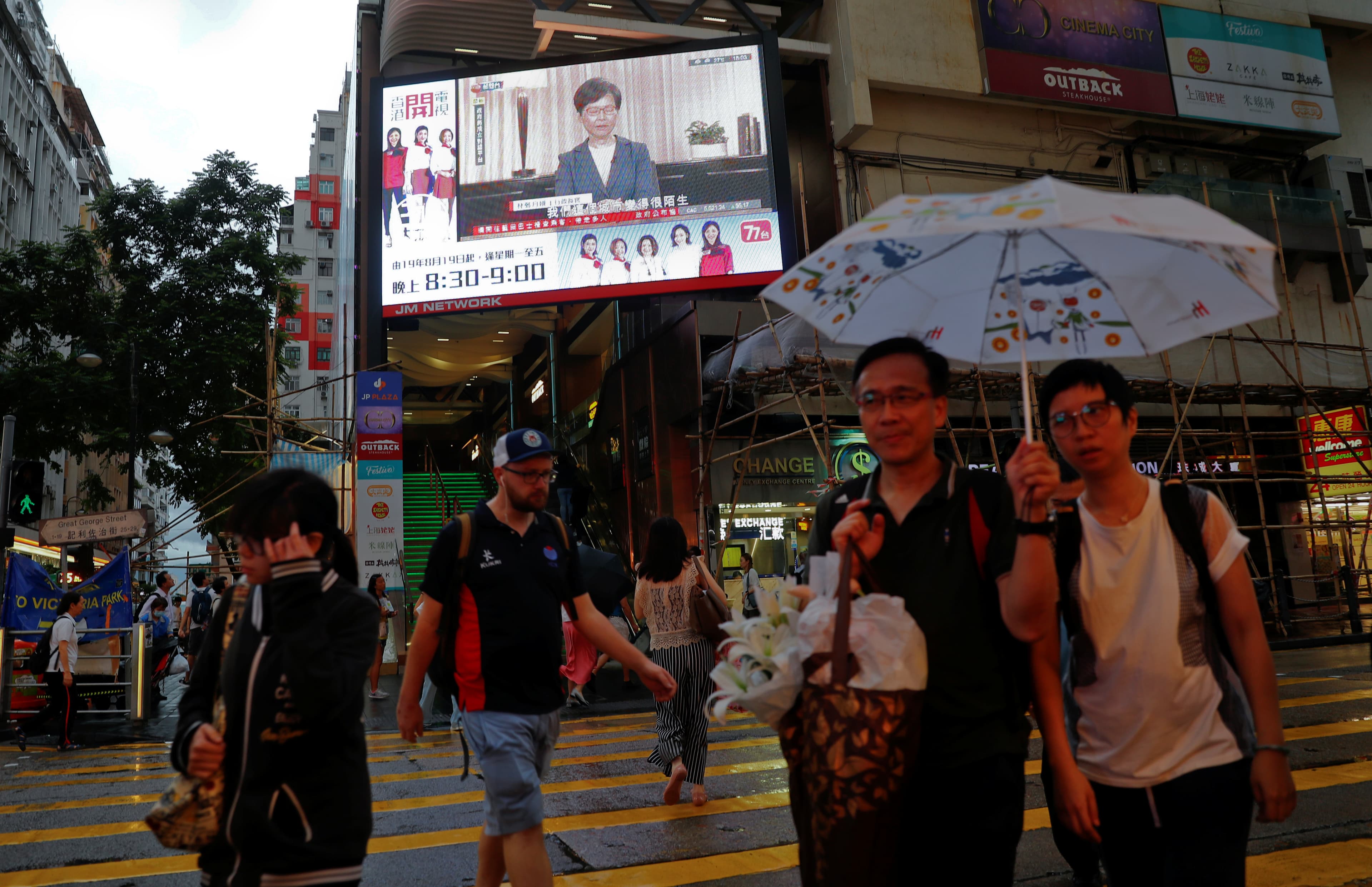 A large television screen elevated above a crosswalk on a street with passersby