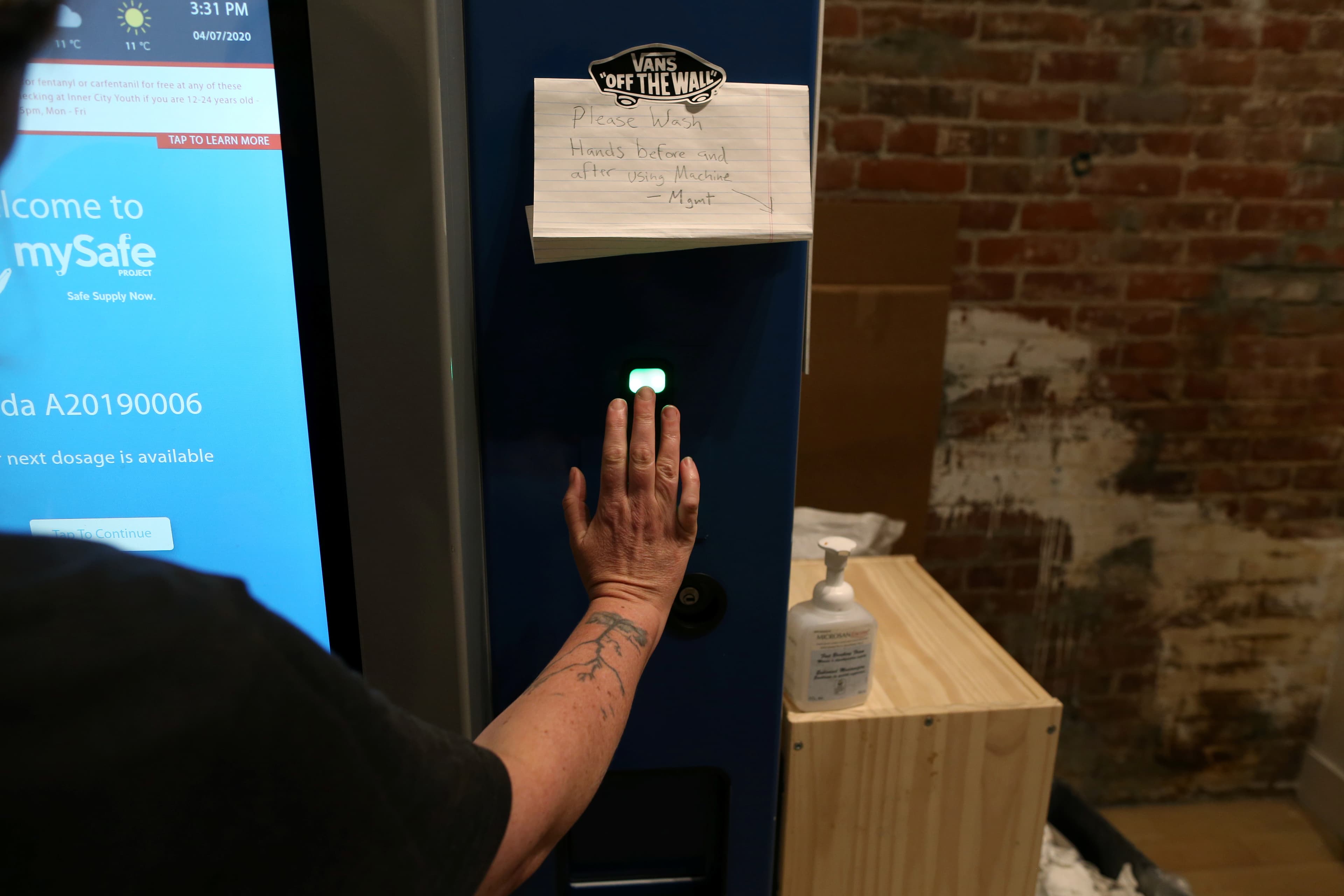 A woman demonstrates how the mySafe narcotic dispensing machine uses a palm-print ID at the Overdose Prevention Society as the local health unit has begun prescribing a