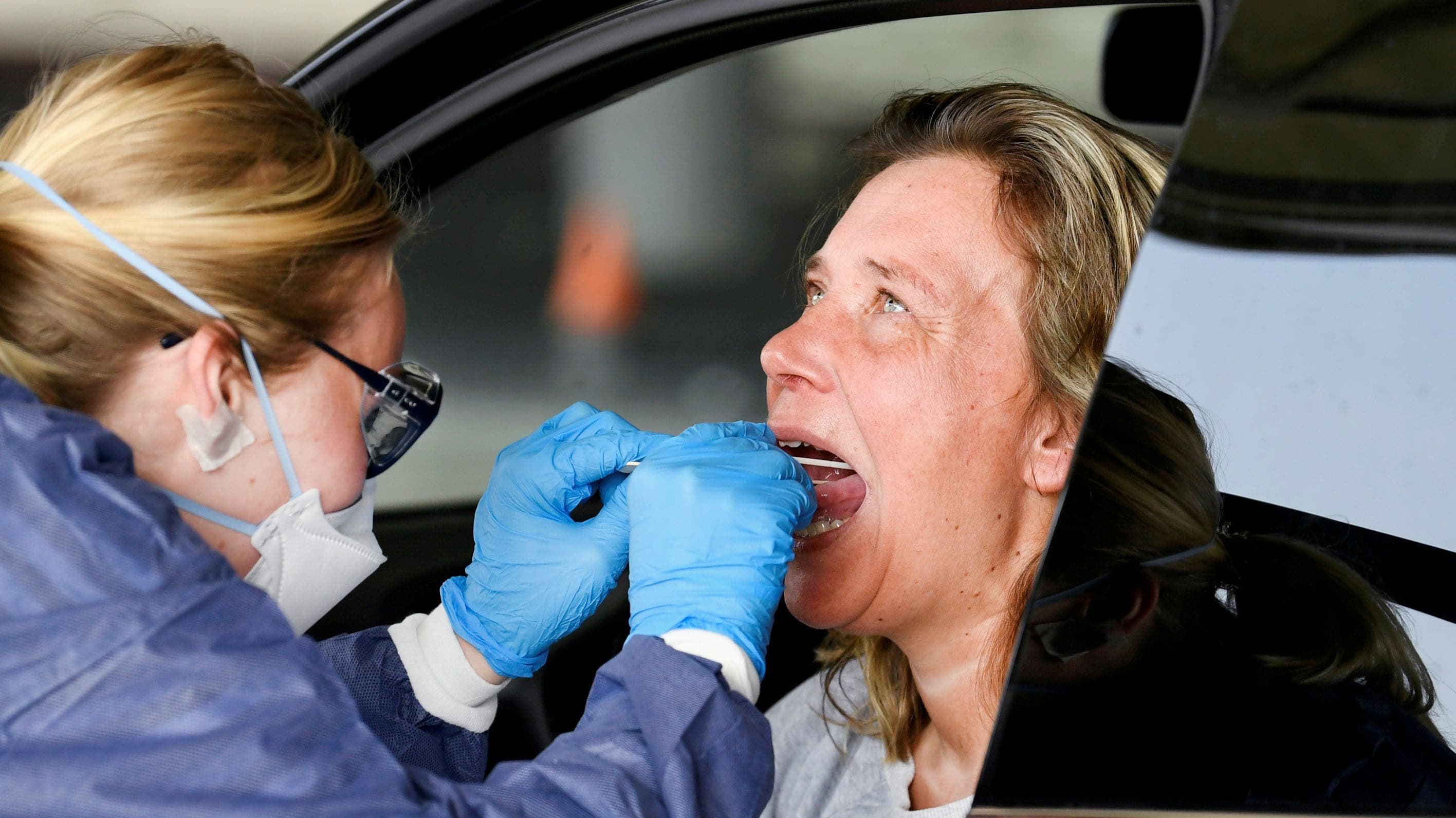 A member of medical staff takes coronavirus test samples of a woman during drive-thru coronavirus disease (COVID-19) testing, on a converted ice rink.