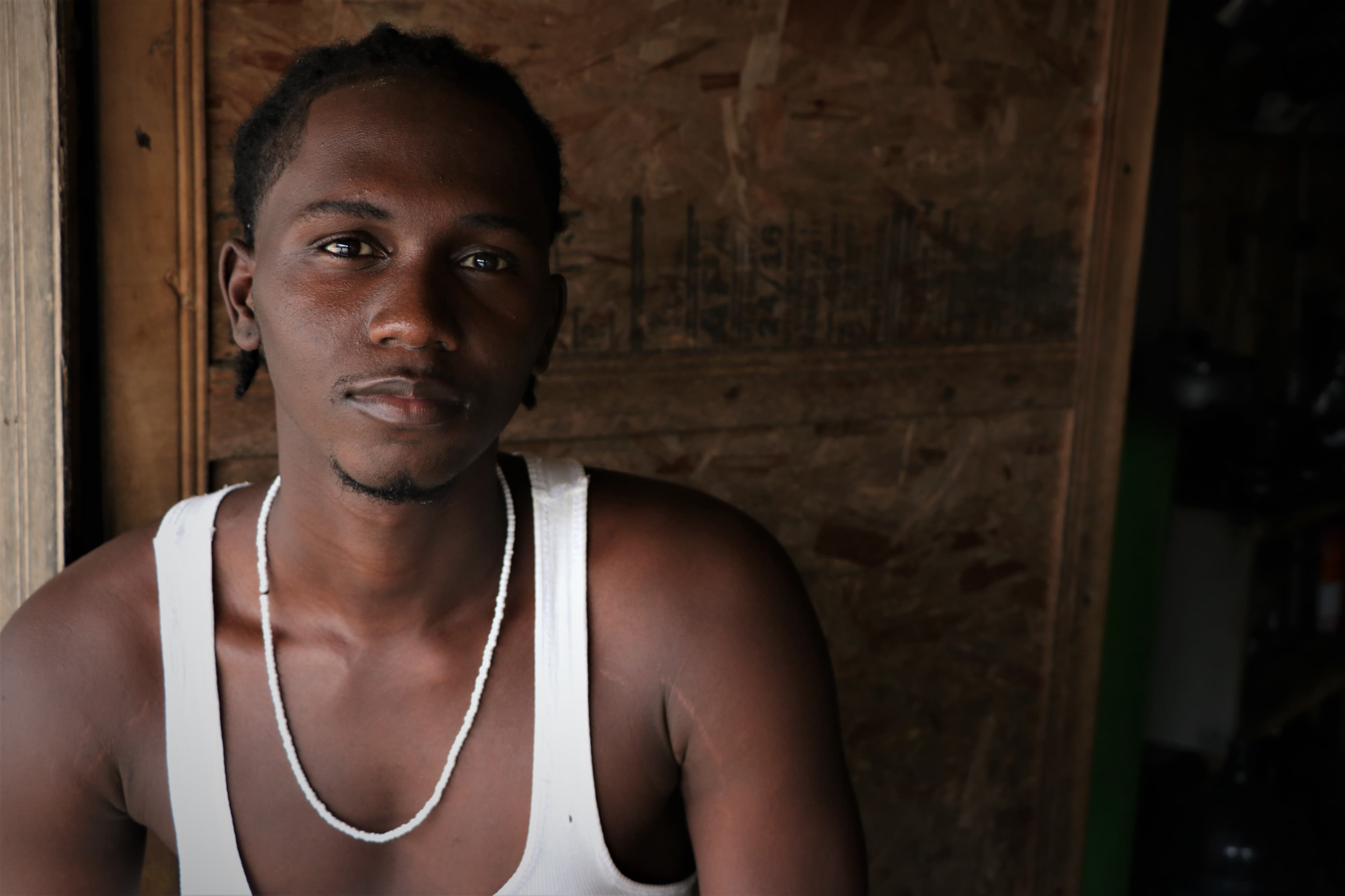 A young man wearing a white tank poses.
