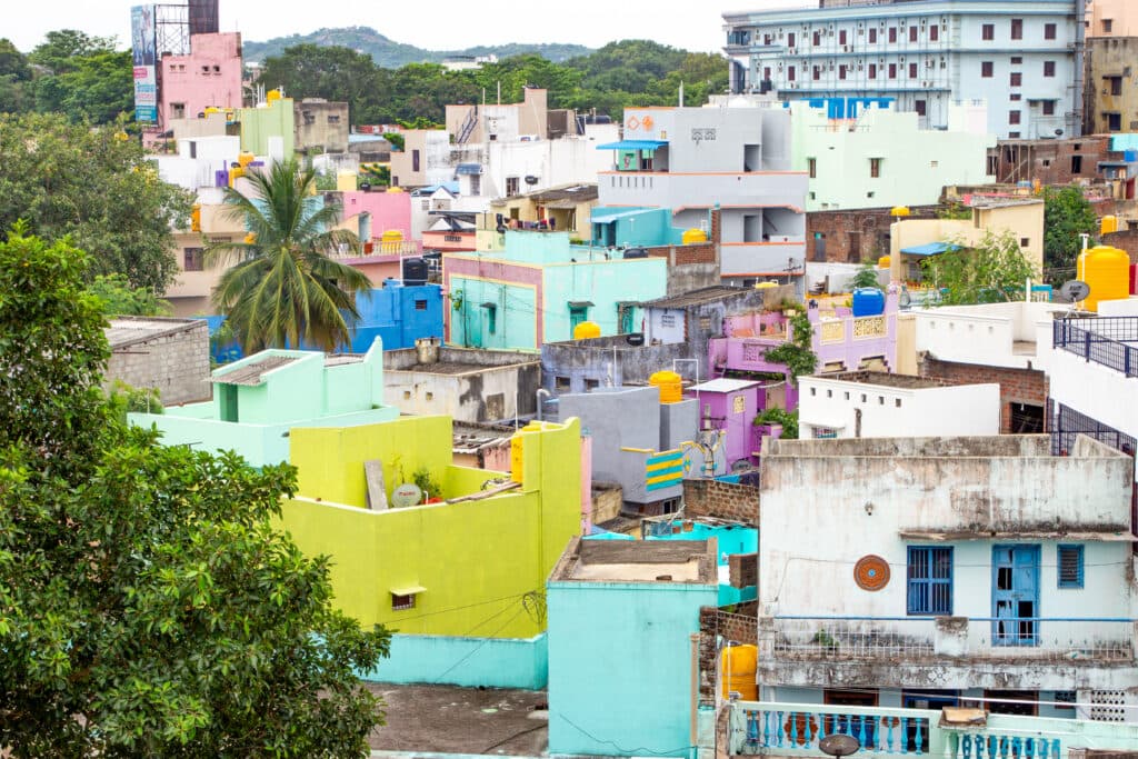 Colorful residential buildings in an urban area, with various shades of green, blue, pink, and yellow, surrounded by greenery and a palm tree.