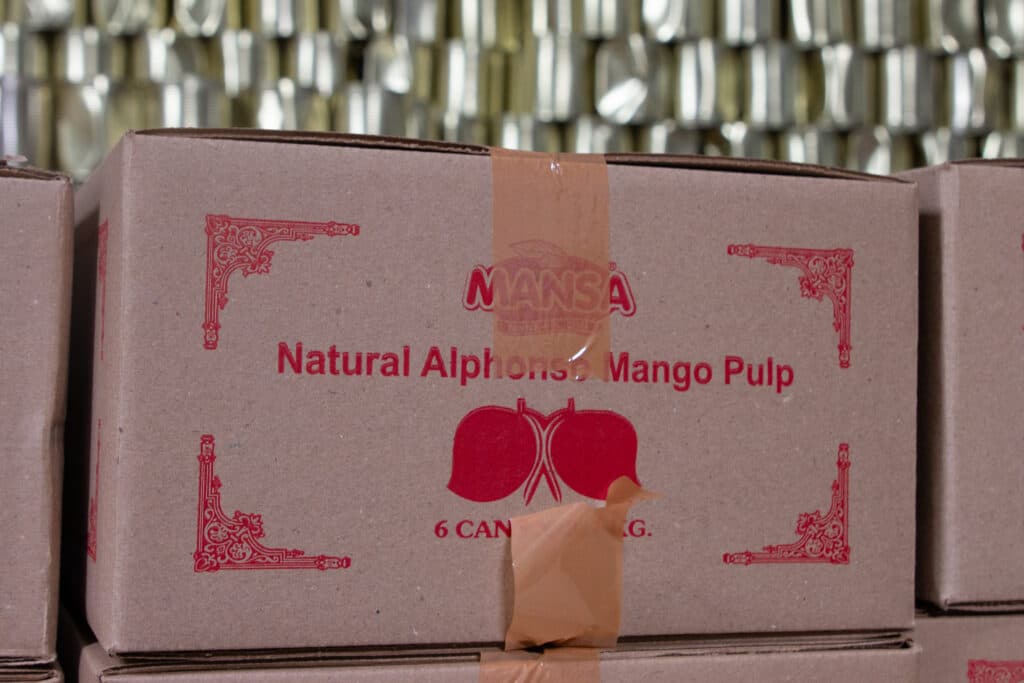 Cardboard boxes labeled "Natural Alphonso Mango Pulp" with decorative red designs and taped seams.