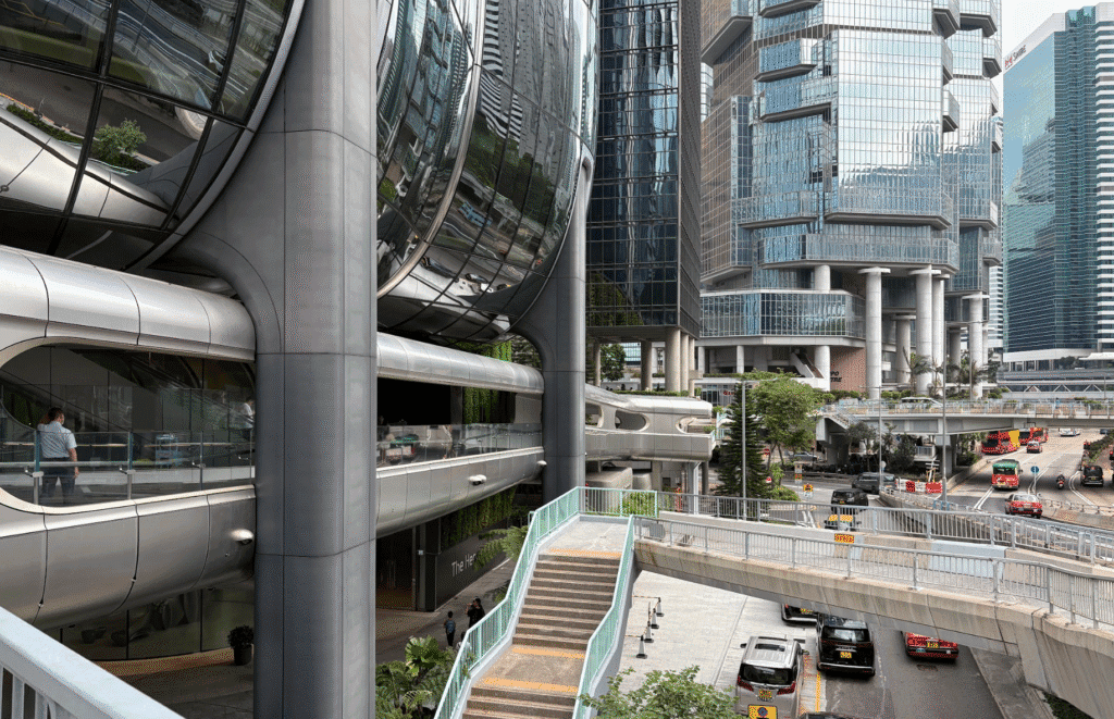 Cityscape view with modern glass and steel skyscrapers, elevated walkways, and a busy street below with vehicles and pedestrians.